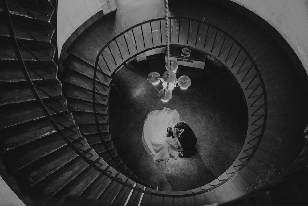 A dramatic black and white spiral staircase photo with a chandelier in the center.
