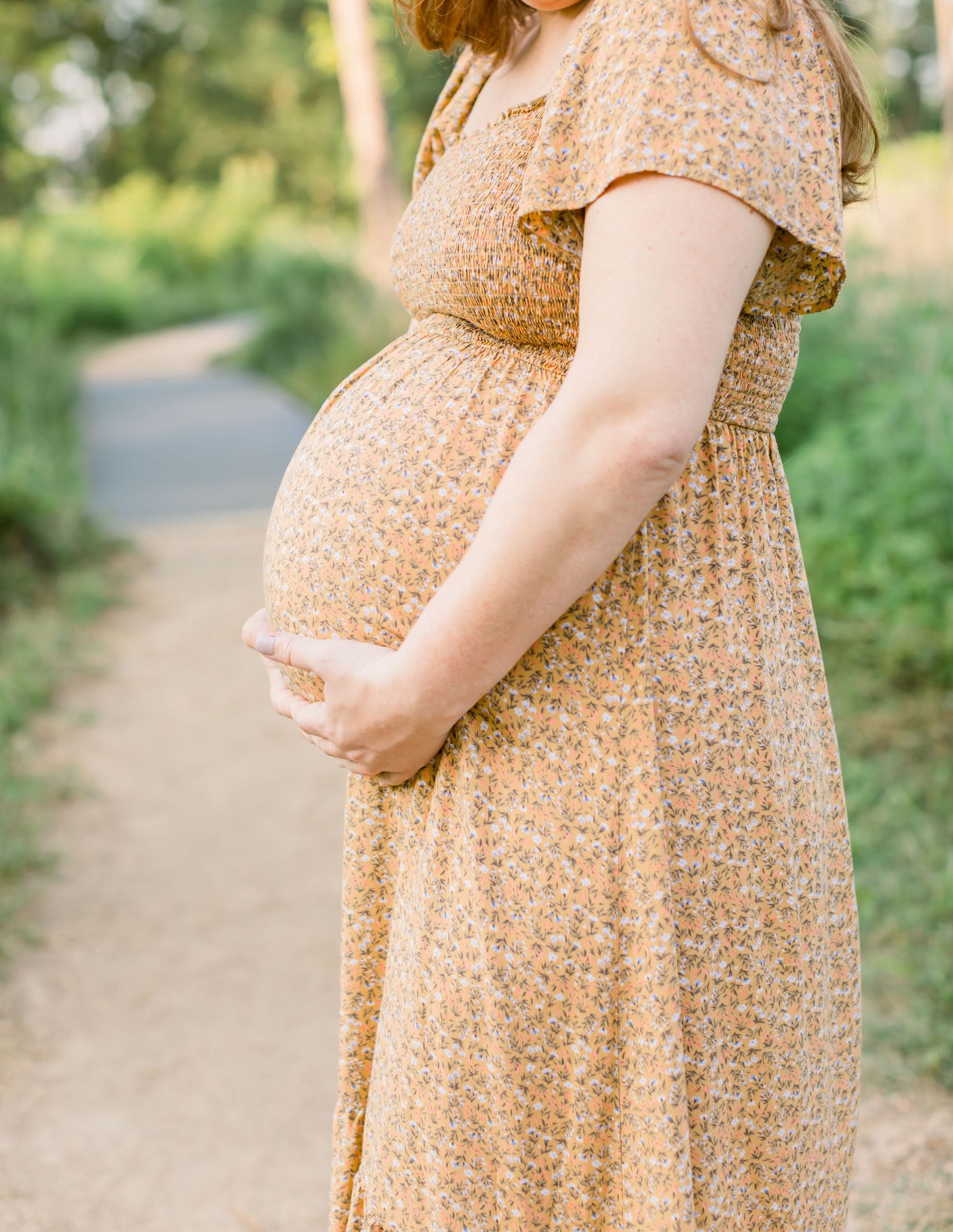 Close-up view of a pregnant belly in a floral peach-colored maternity dress on a walking path.
