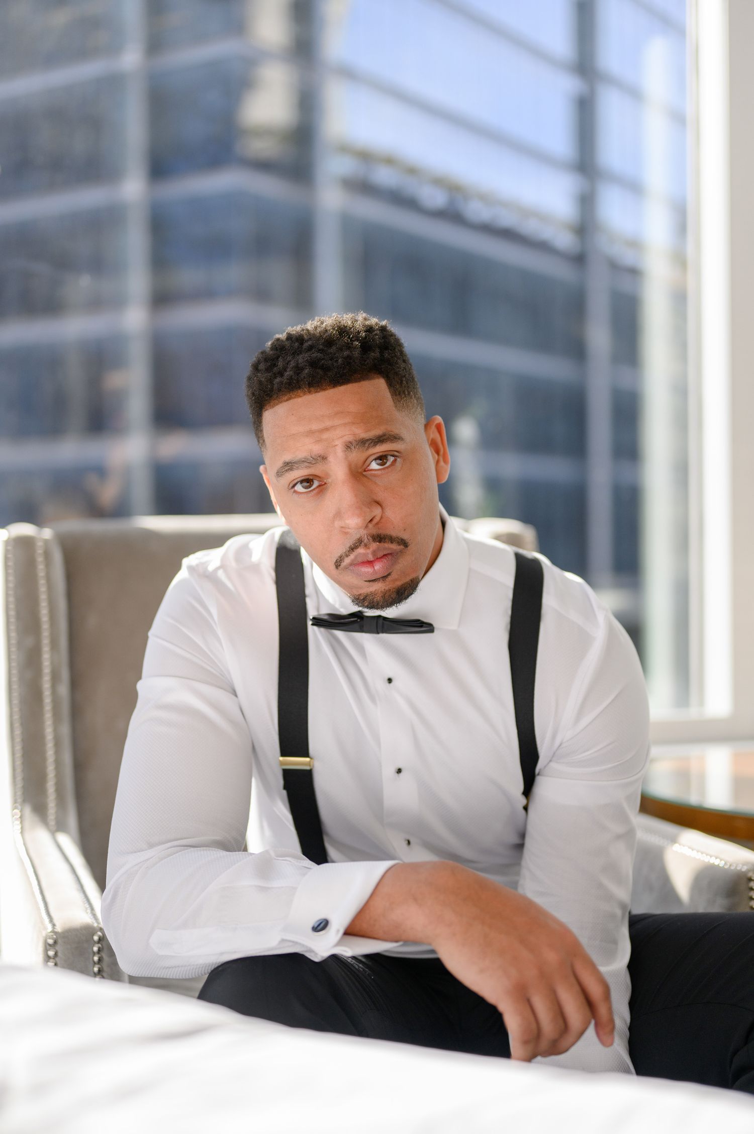 Well-dressed person in white shirt and suspenders sitting thoughtfully in modern setting.