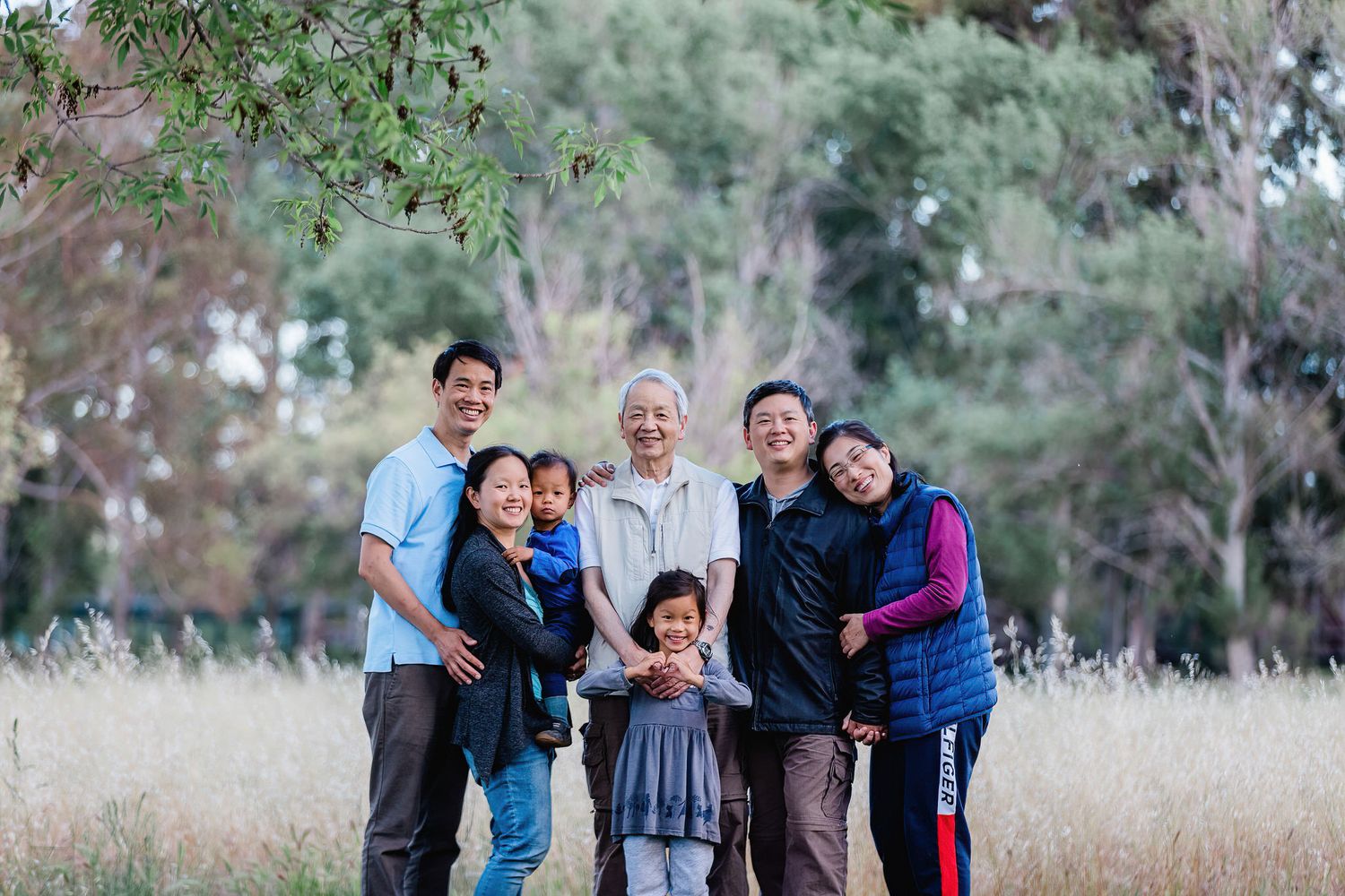 Extended family gathering outdoors for a group photo in a natural setting with tall grass.
