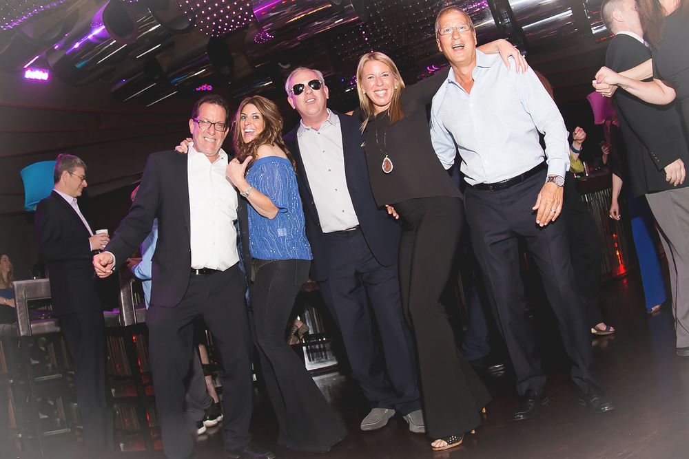 Group of party guests dancing and celebrating under purple lighting at nightclub event.