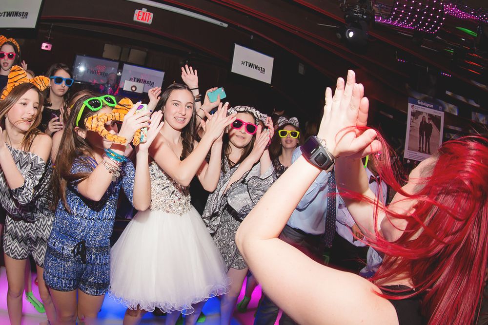 Wedding party and guests dancing enthusiastically on a nightclub dance floor with colorful lighting.