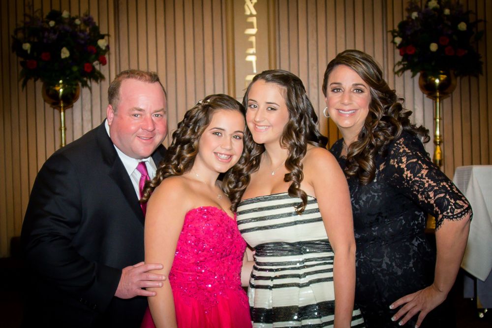 Group photo of four people in formal attire at a festive party with decorative wreaths in background.