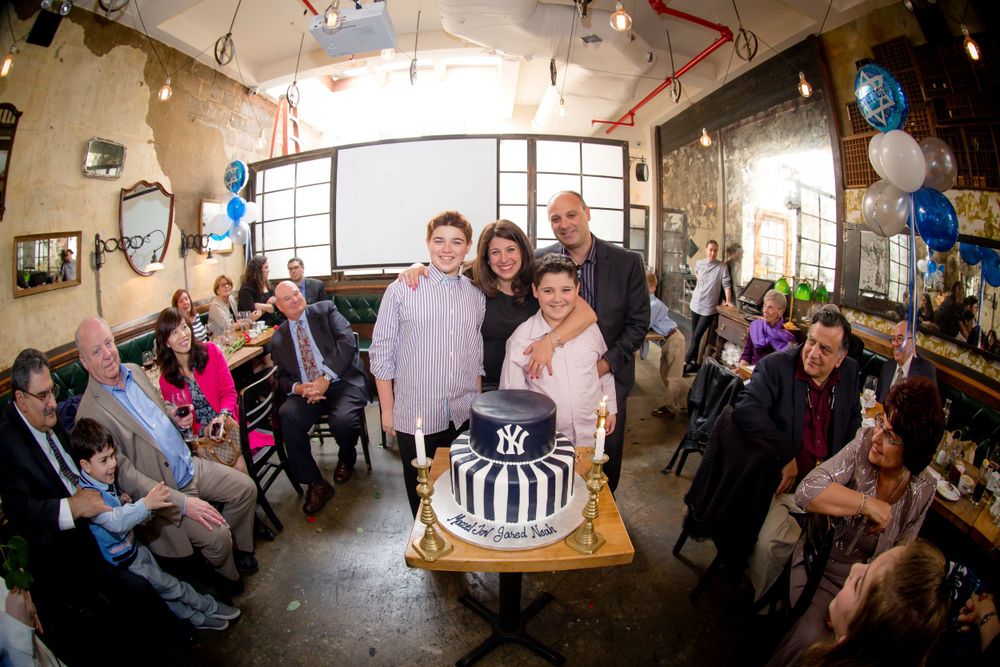Celebration scene with black and white cake surrounded by party guests in casual setting.