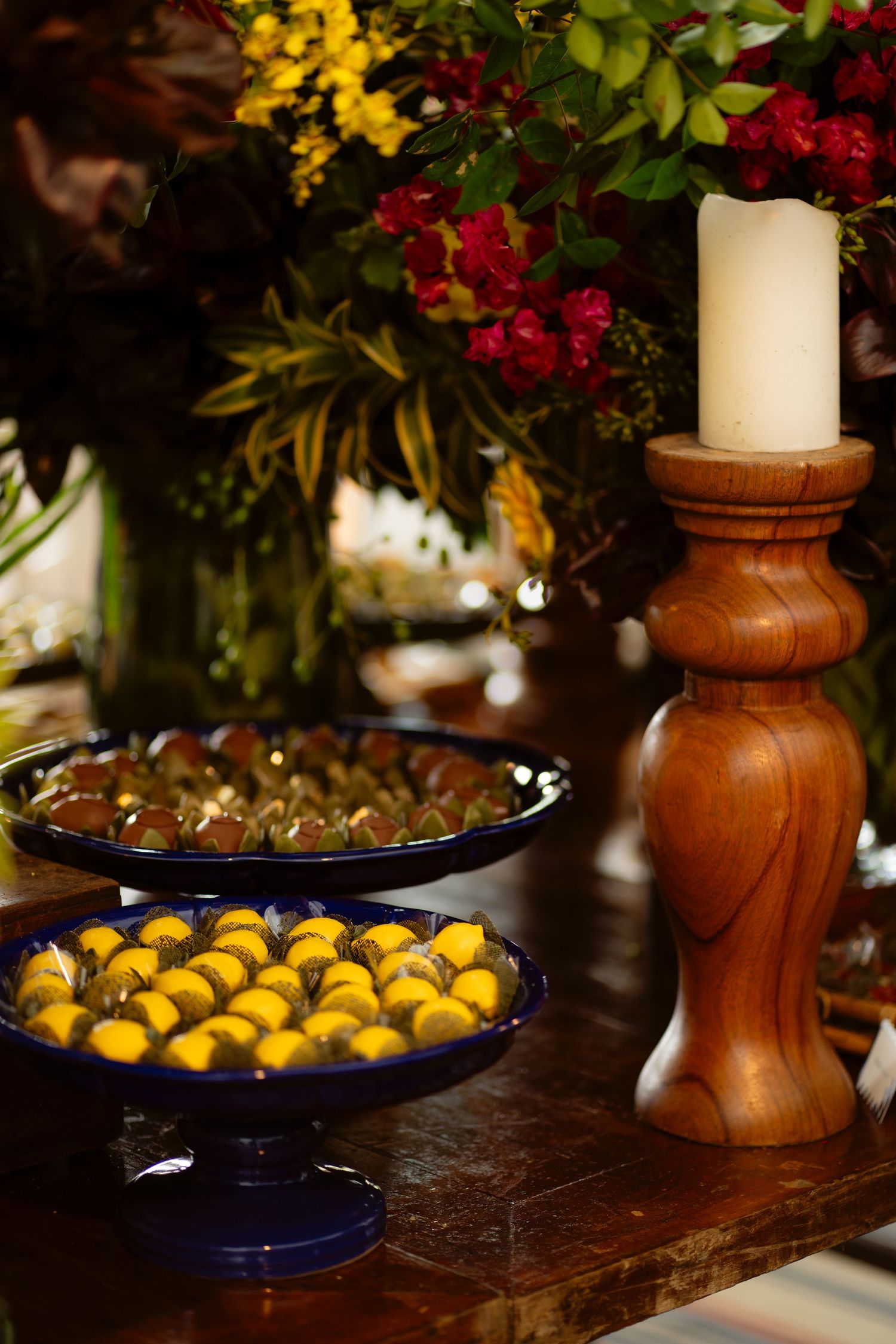 Rustic wooden candlesticks and navy blue serving platters with fruit arranged among colorful floral decorations.