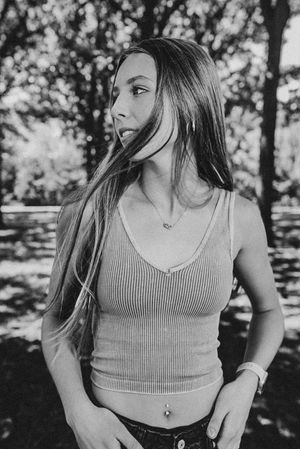 Black and white portrait of person in tank top with long hair in outdoor setting.
