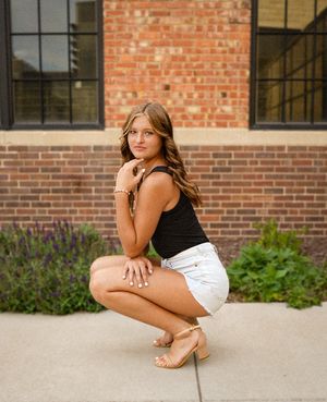 Portrait of a person in black top and white shorts squatting against brick building.