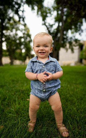Happy toddler wearing denim outfit standing on grass outdoors.