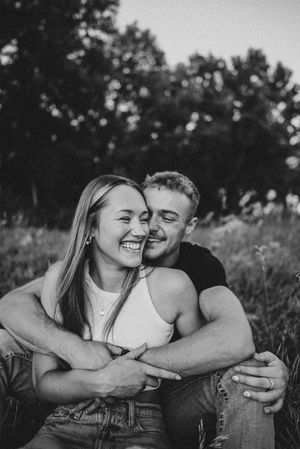 Black and white photo of couple embracing and laughing in field.