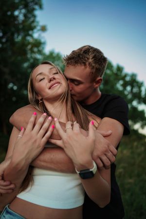 A romantic outdoor photo captures an intimate embrace against a blue summer sky.