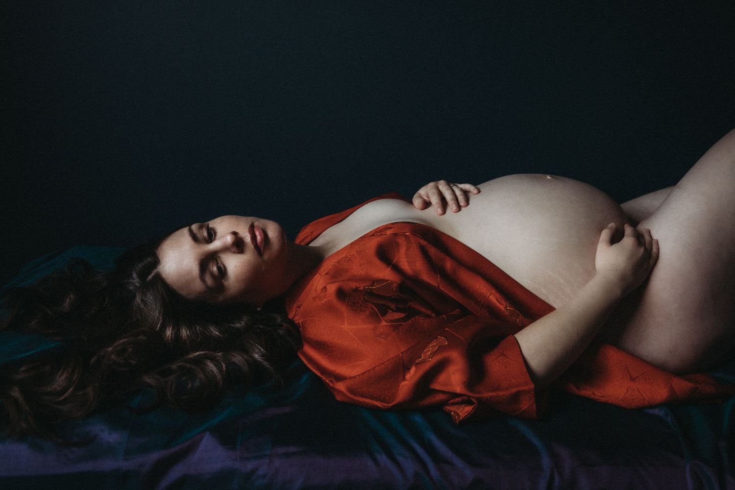 award winning maternity photography by sarah stirk london of pregnant woman laying on couch in red robe