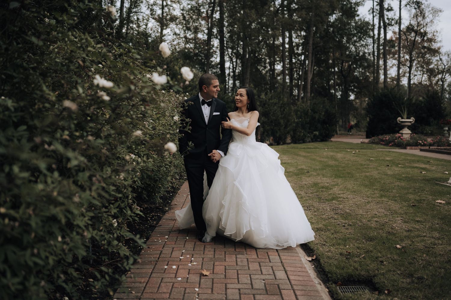Newlyweds walking together along a brick pathway surrounded by lush greenery.