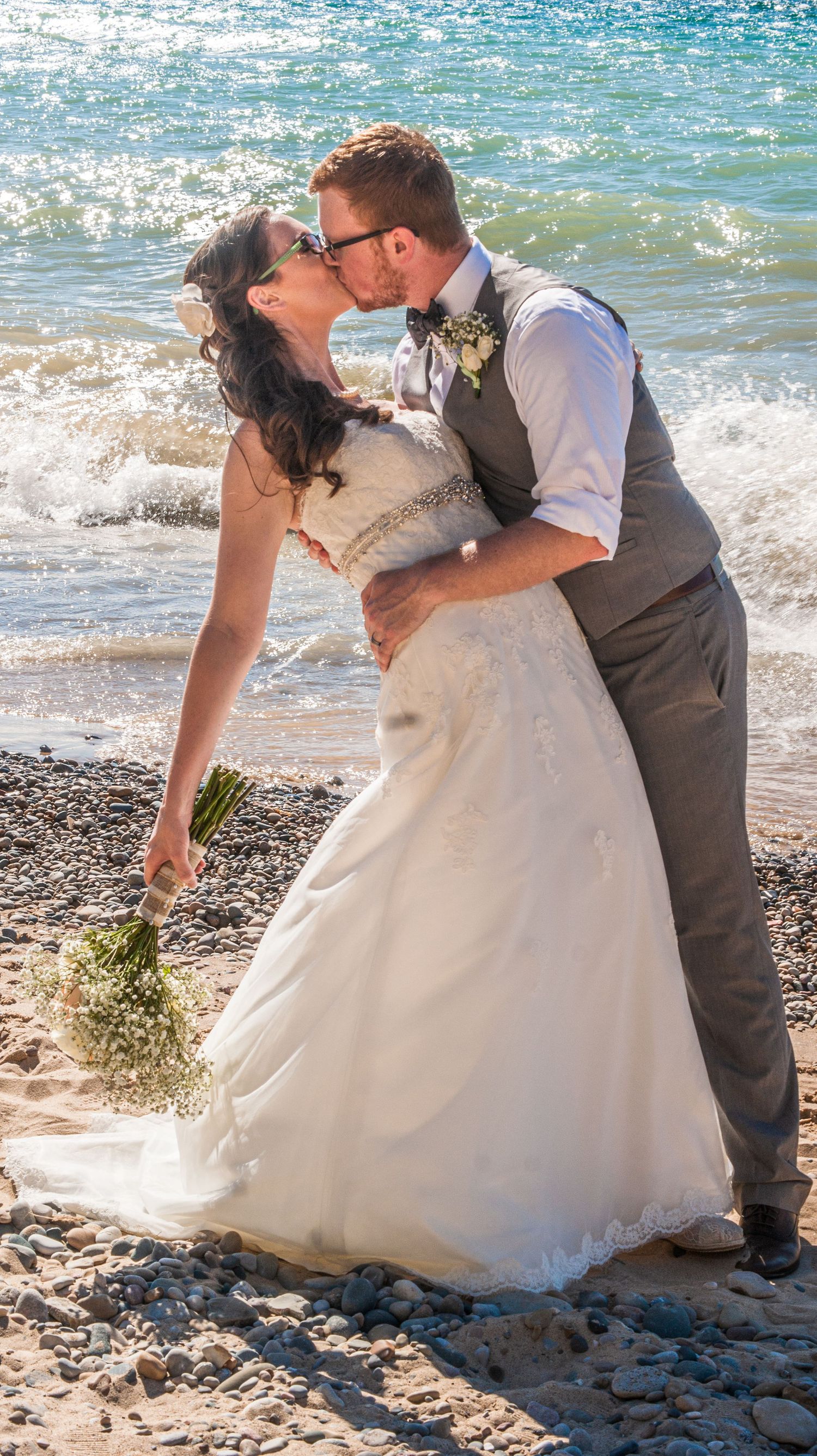 Wedding couple sharing romantic moment on beach with waves crashing behind them.