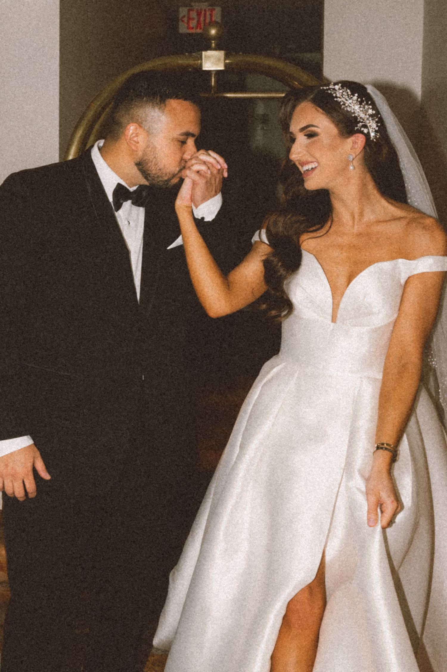 Sweet moment between newlyweds in formal attire under hallway lighting.