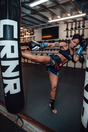 Martial artist executing high kick against heavy bag during training session.