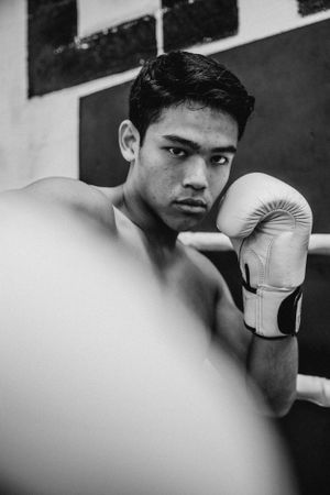 Black and white portrait of a boxer in defensive stance wearing white gloves in a gym setting.