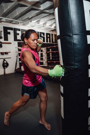 Fighter practicing powerful kicks on a heavy bag in a training gym.