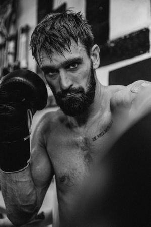 Dramatic black and white portrait of boxer wearing gloves in training gym.
