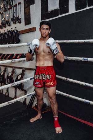 Fighter in red Muay Thai shorts resting between rounds in boxing ring.