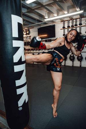 Fighter practicing low kicks on heavy bag during intense training session.
