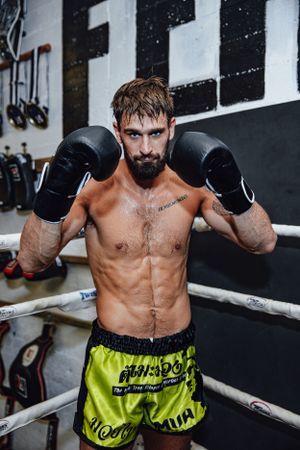 Athletic boxer in yellow shorts and black gloves stands in fighting stance in boxing ring corner.