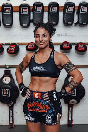 Martial artist posing with boxing gloves against wall of training equipment.