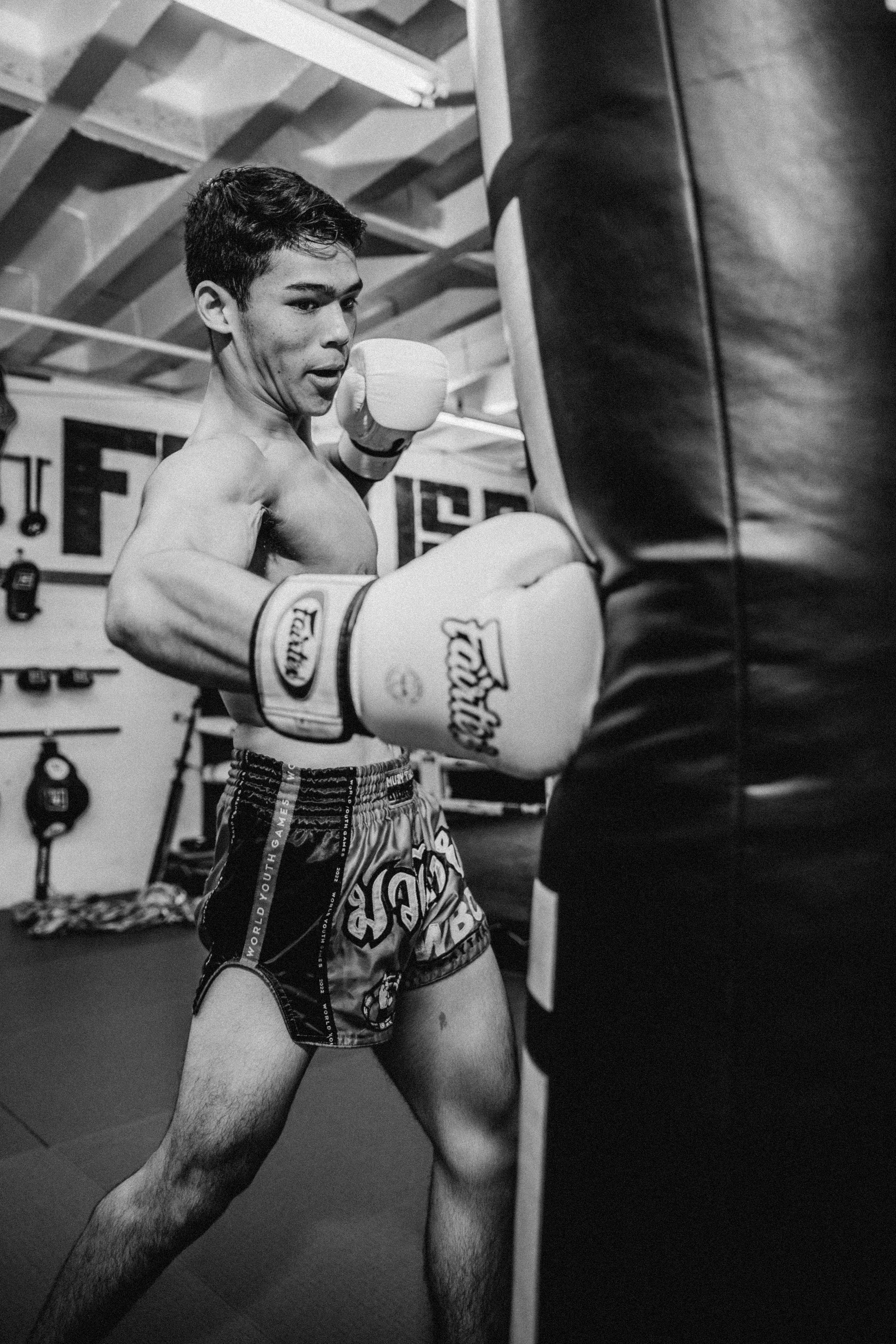 Muay Thai fighter practicing strikes on a heavy bag in black and white.