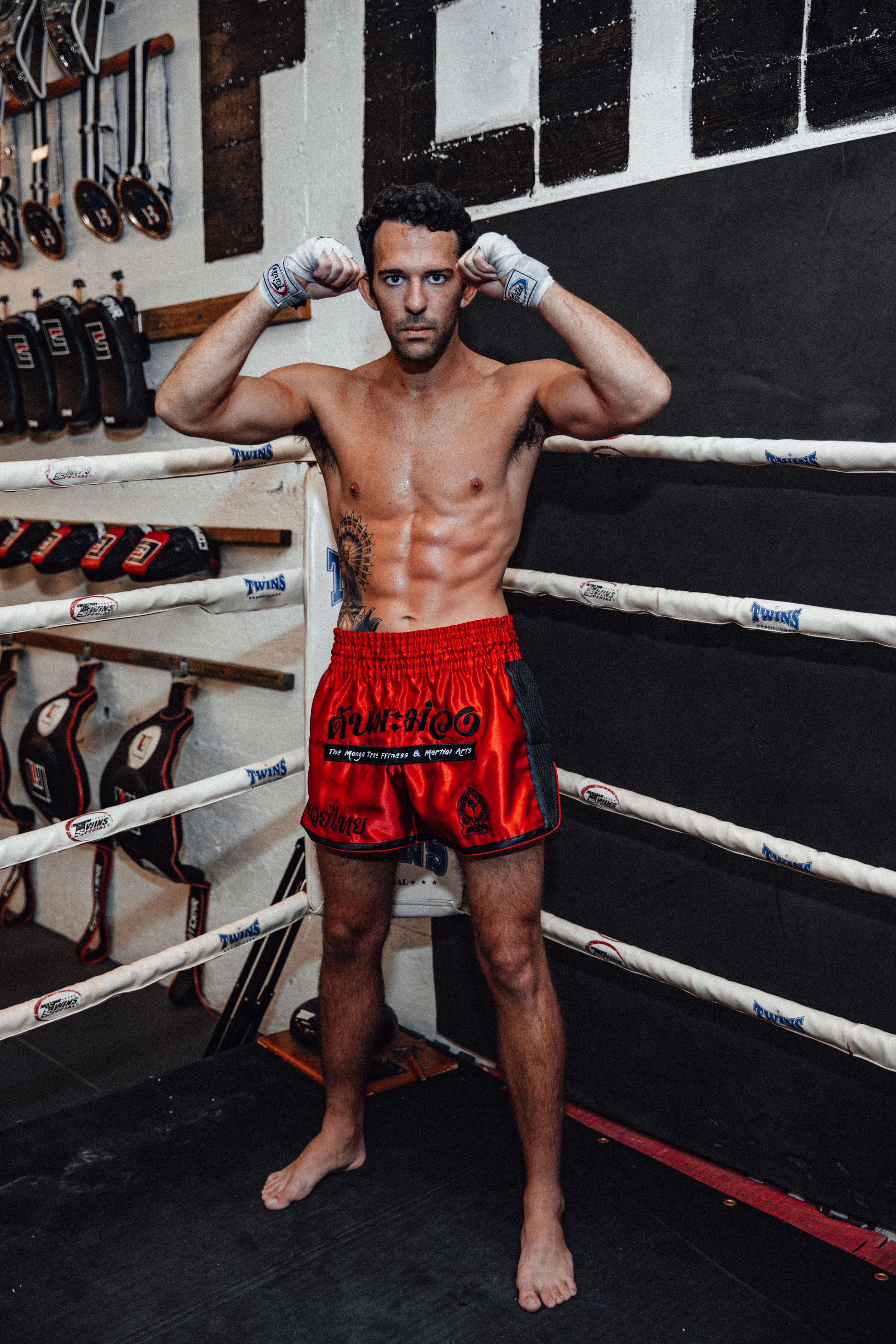 Athletic fighter in red shorts demonstrating boxing stance in a training ring.