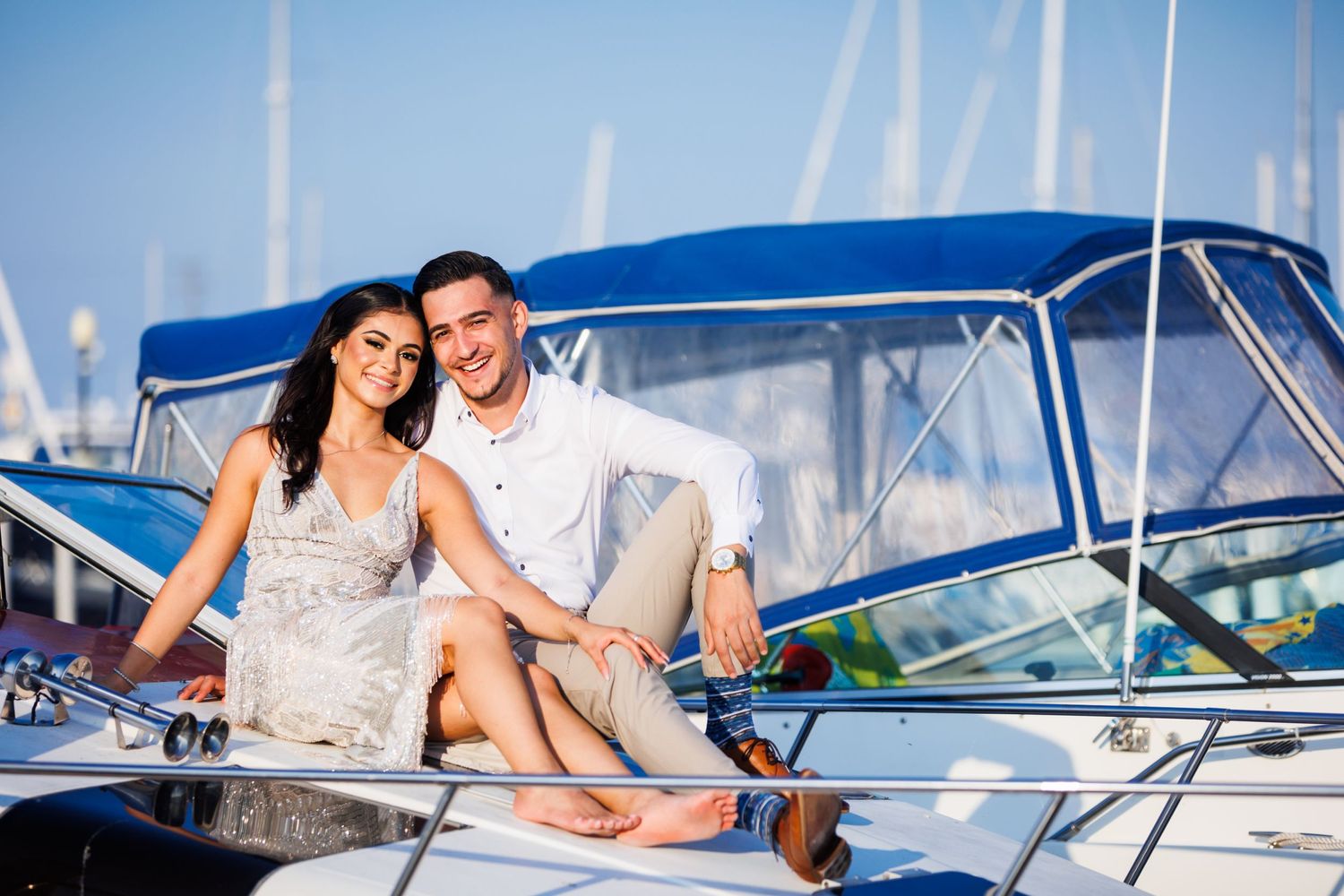 A couple enjoying a romantic moment on a yacht with sailboat masts visible in the background at a marina.