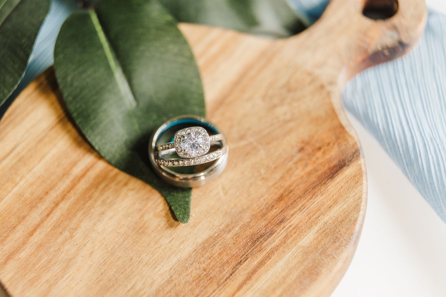 Diamond engagement ring photographed on a wooden board with a tropical monstera leaf.