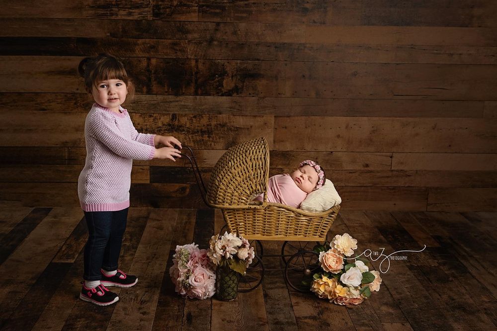 Rustic wooden scene with wicker basket, pink flowers and two siblings sharing a tender moment.