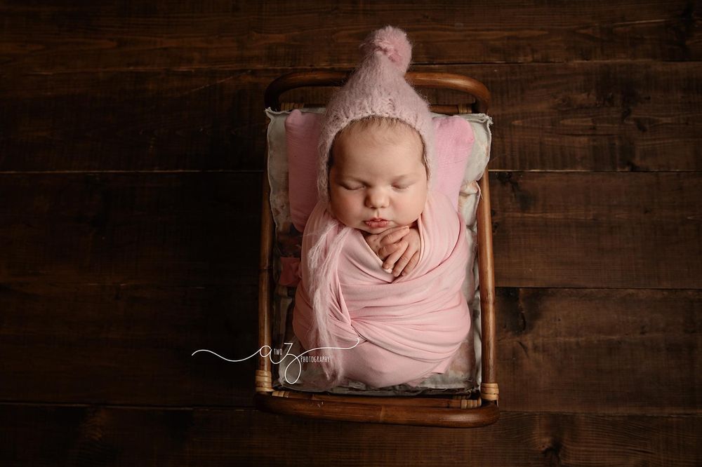 Sleeping baby wrapped in pink swaddle posed in vintage wooden drawer.