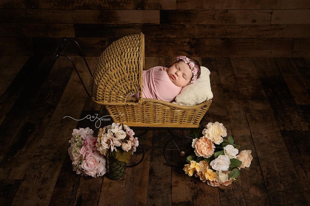 Wicker basket with pink floral arrangements on wooden floor in warm studio lighting.