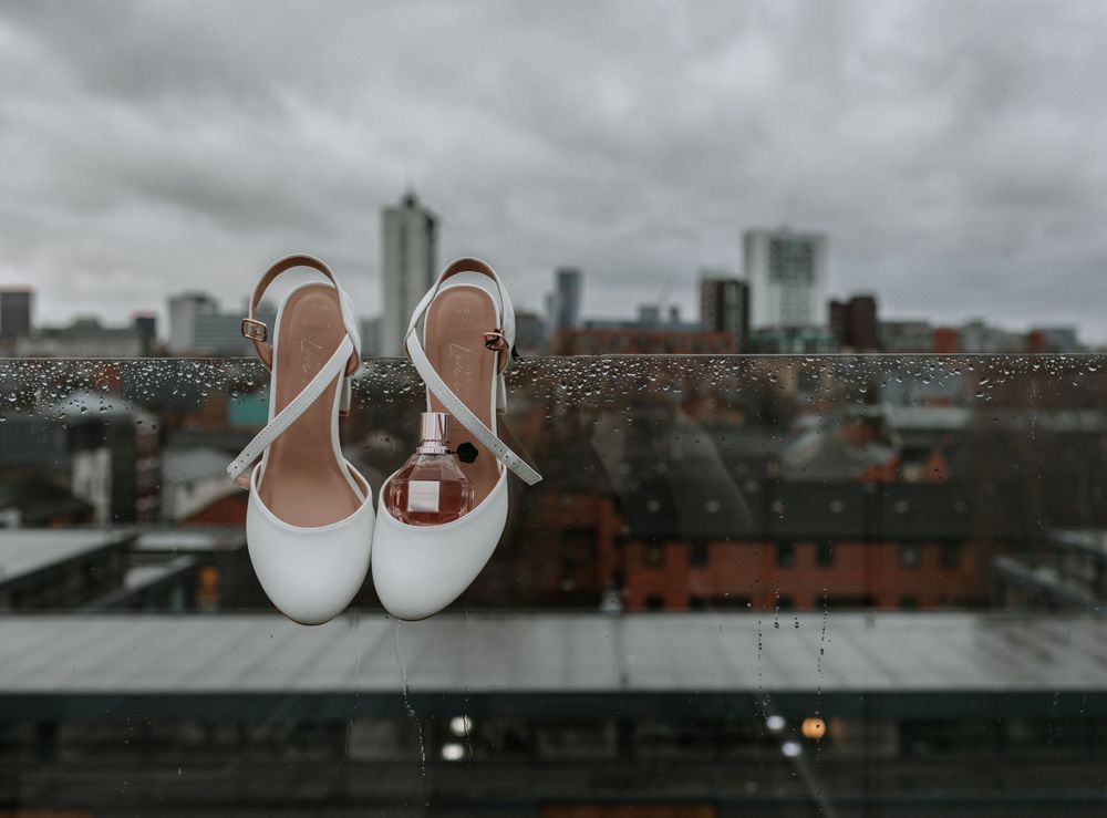 White bridal shoes and wedding rings arranged against urban skyline backdrop.
