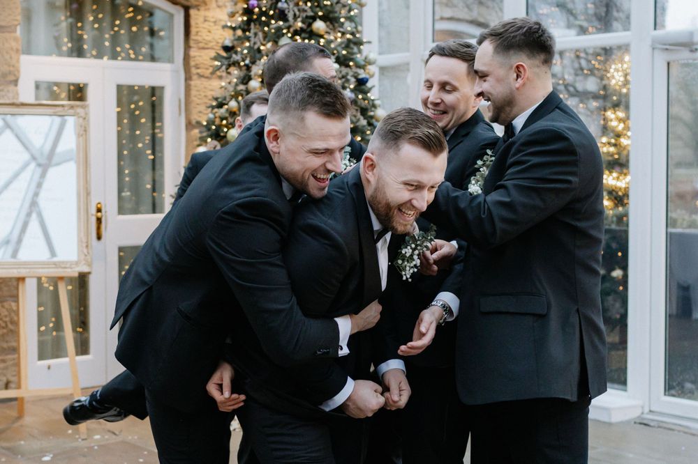 Groomsmen in black tuxedos sharing laughs and candid moments at wedding reception.