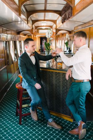 A groom and his best man enjoys a whisky in the bar car.