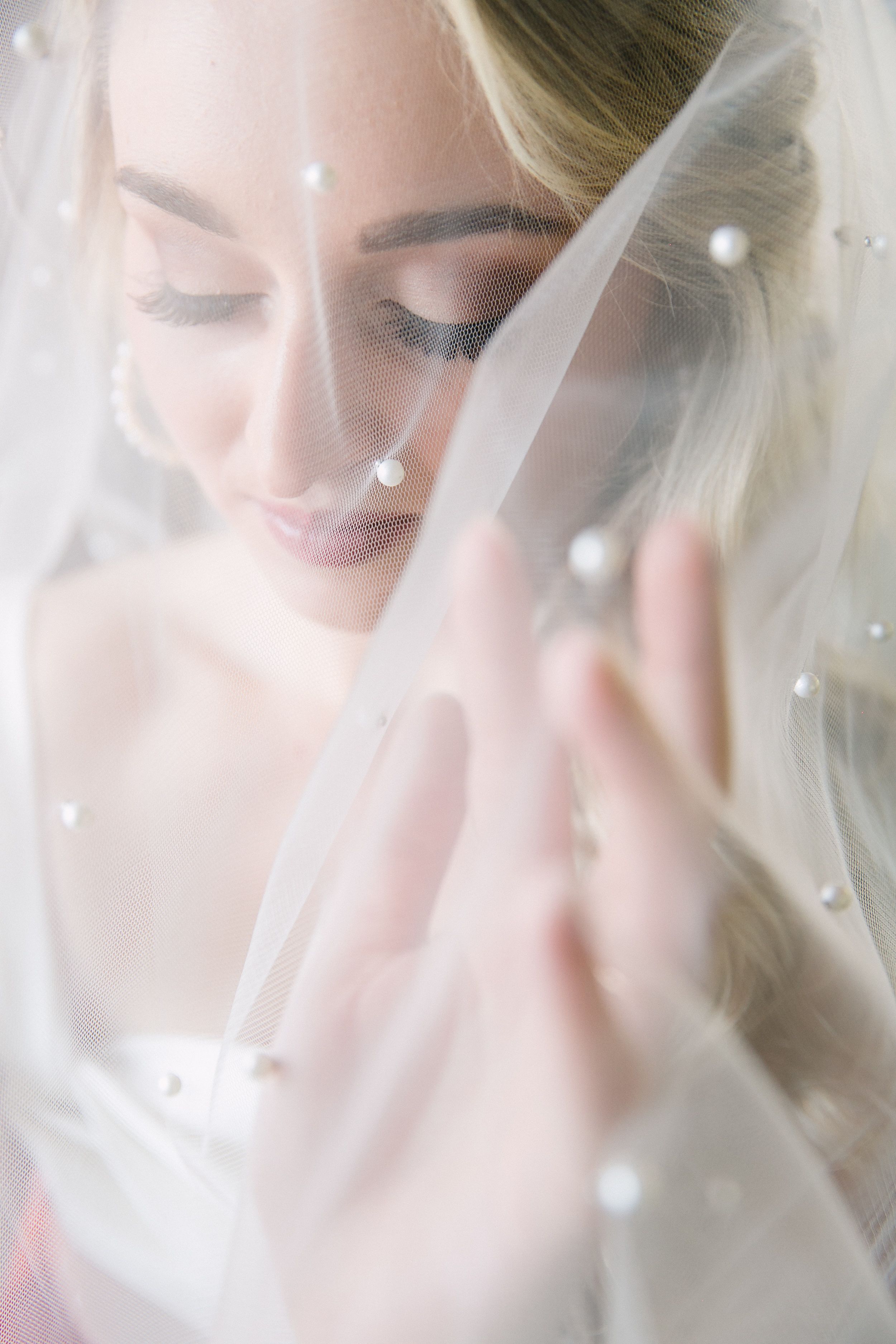 A bride's face hidden behind her veil covered in pearls.