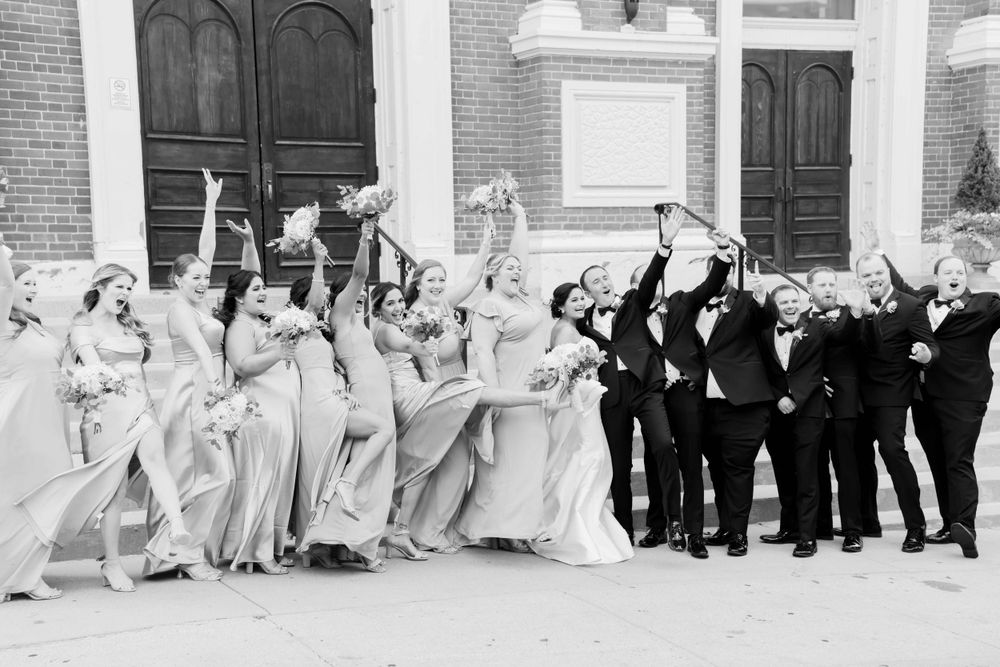 Fun black and white photo of wedding party posing playfully outside brick building.