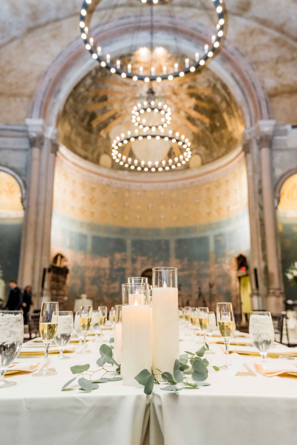Elegant wedding reception table with glowing candles and chandeliers in historic domed venue.