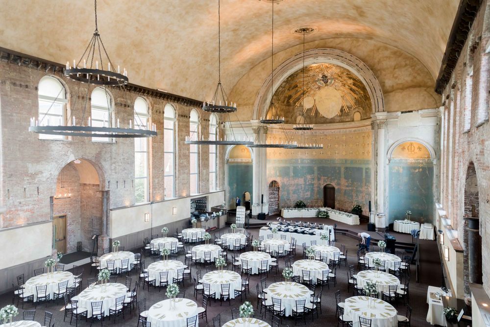 Historic venue with arched ceilings, chandeliers and round tables set for an elegant reception.
