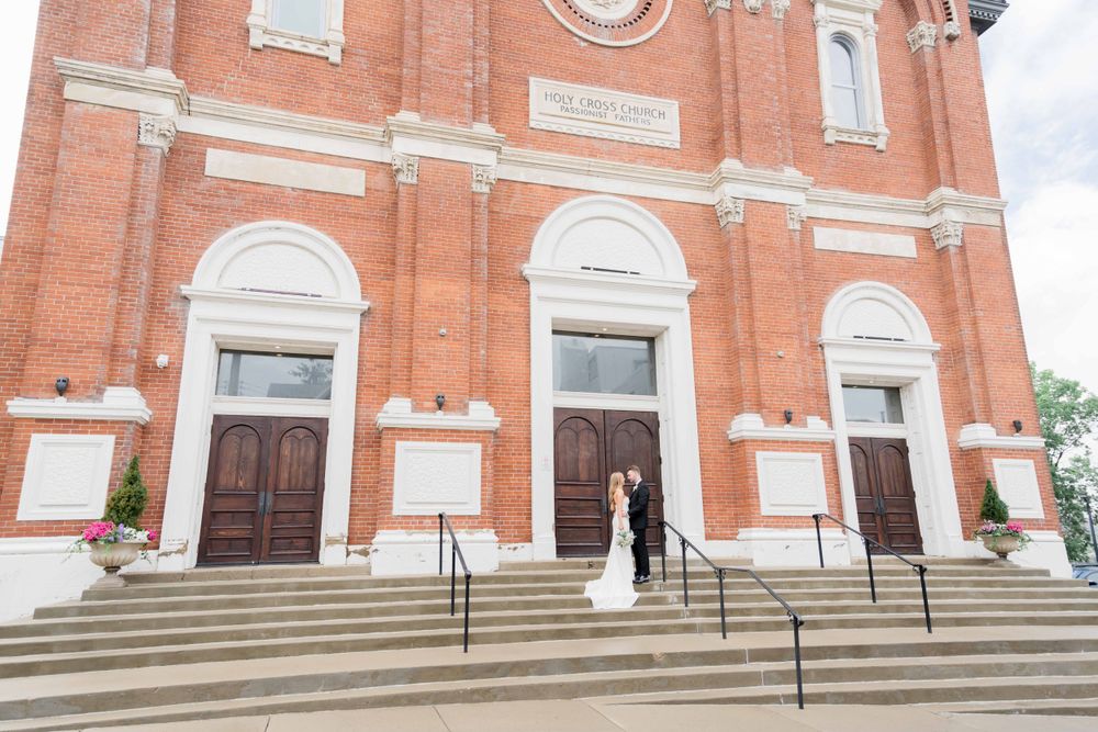 Wedding couple standing on steps of historic brick church with classic architecture.
