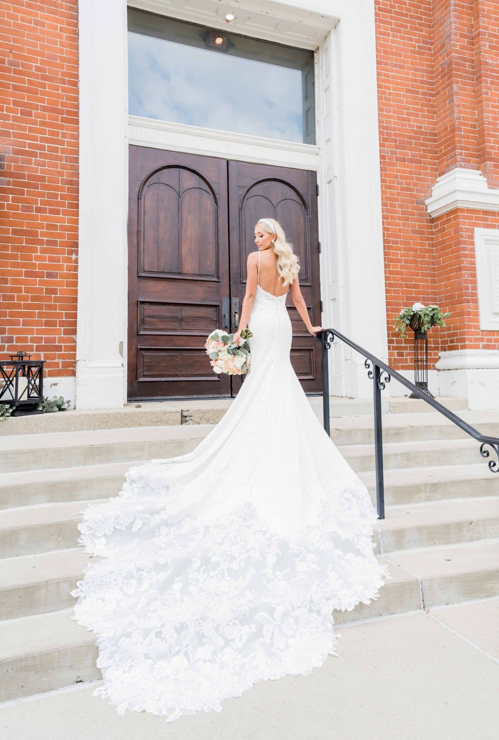 Dramatic cathedral train wedding dress on steps of brick church building.