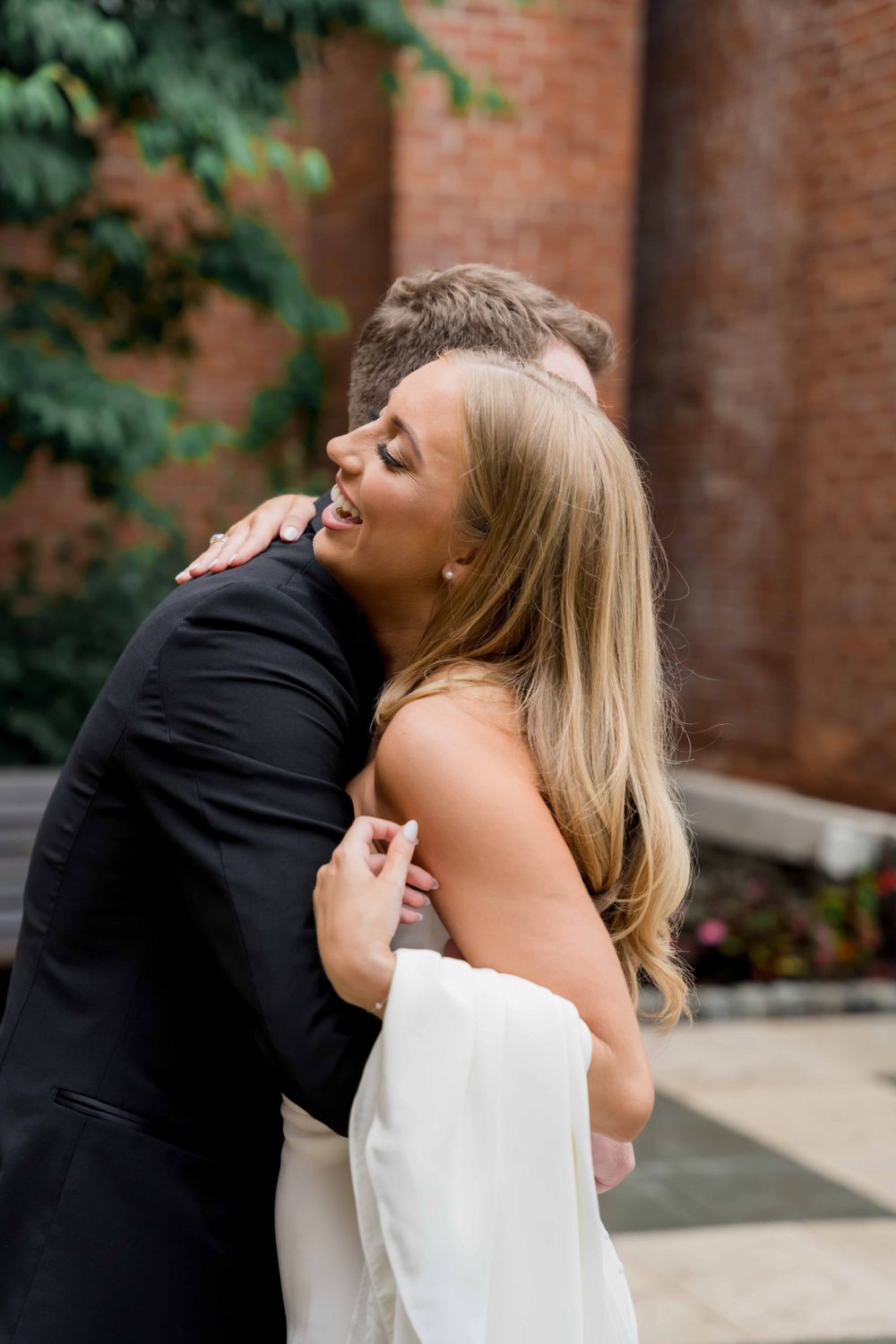 Intimate embrace between newlyweds outside a brick building on their wedding day.