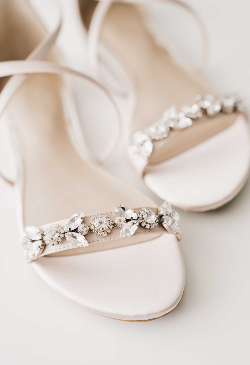 Elegant bridal sandals with crystal embellishments on white straps against a neutral background.