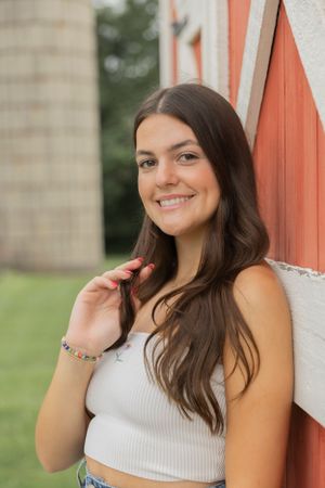 teenage girl leaning against a red barn at cranberry lake park and smiling for a photo