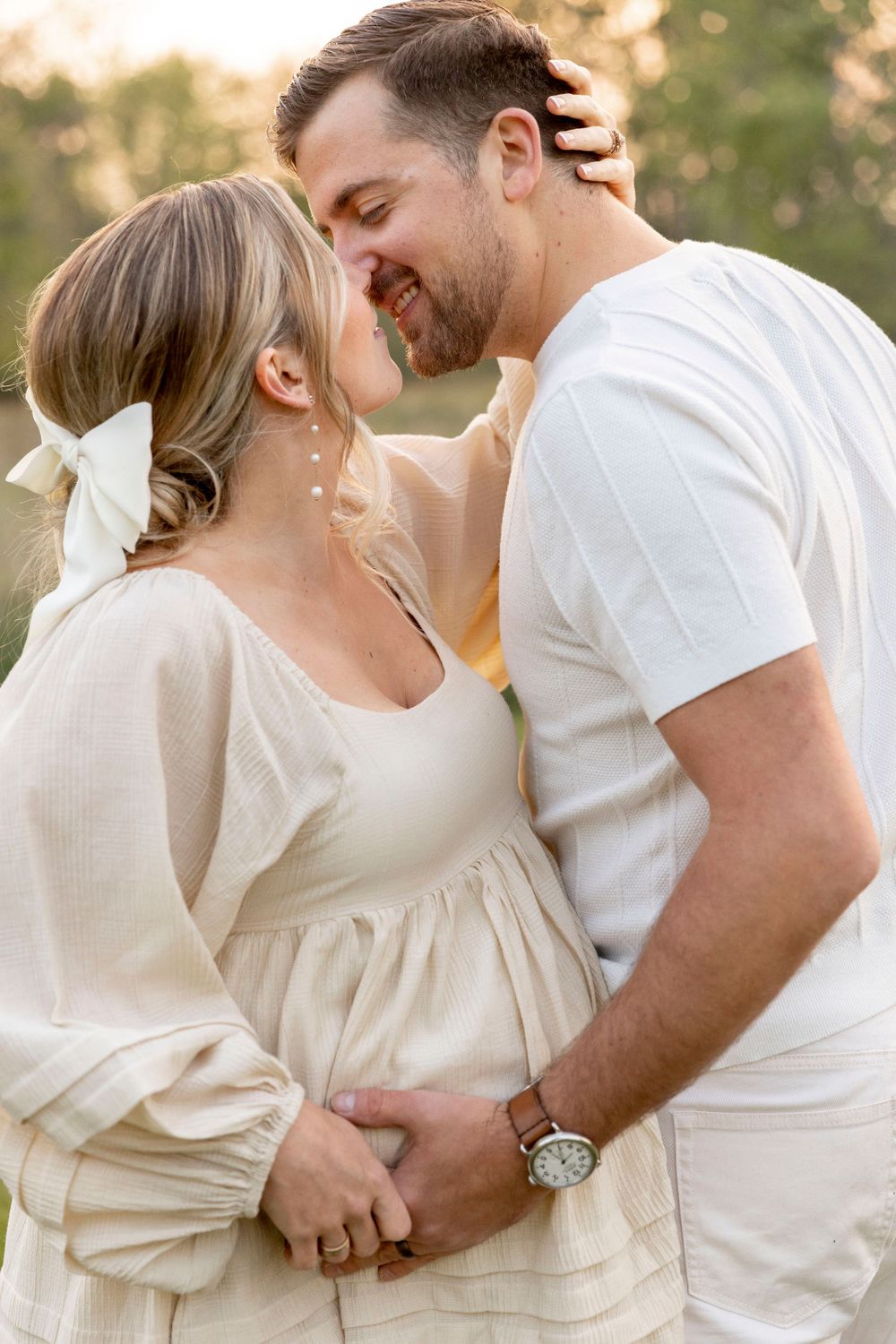 pregnant wife and husband wearing cream and kissing at sunset