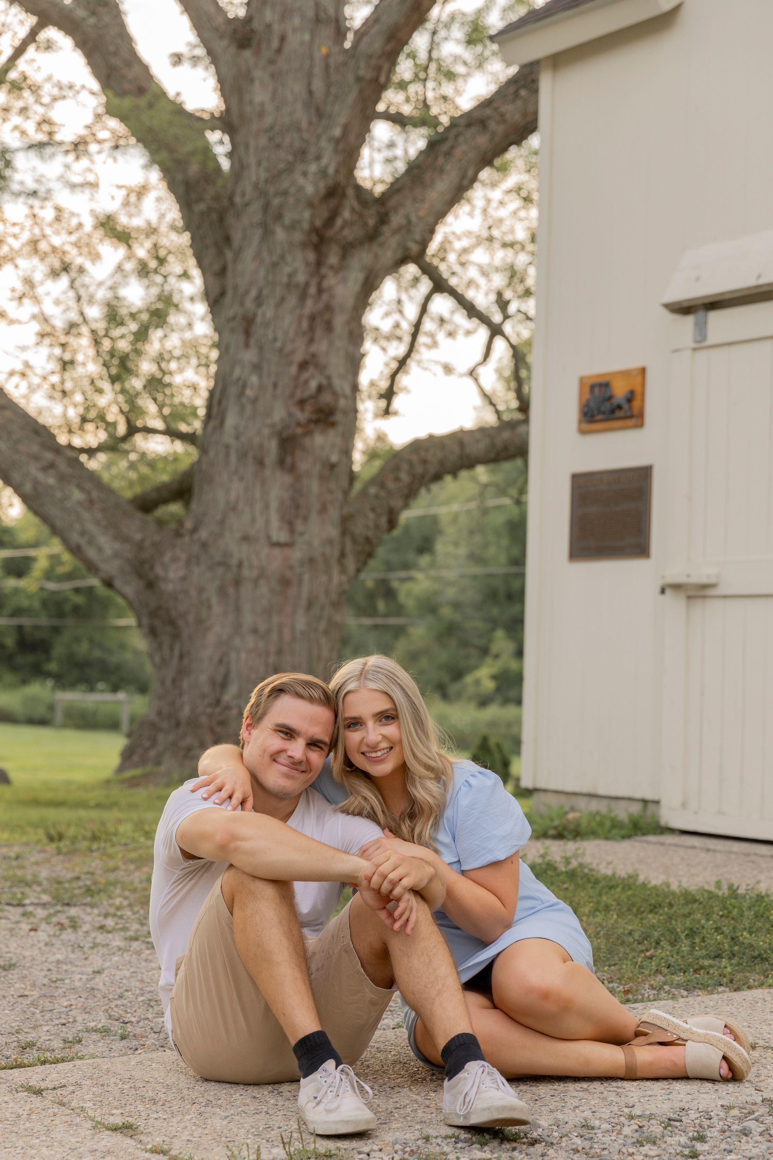 young couple sitting together in front of a white barn in Rochester michigan