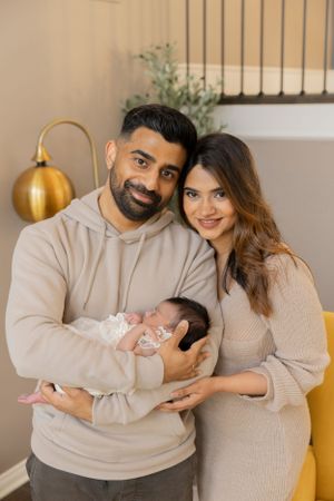 new parents holding their newborn baby girl in cream and beige outfits inside their Shelby township Macomb county home