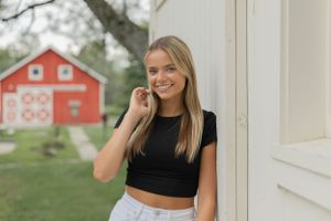 teenage girl leaning against a white barn and tucking her hair behind her ear