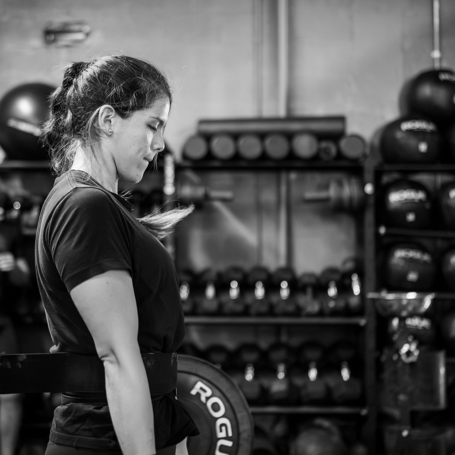 Weightlifter in training gym standing near rack of kettlebells in black and white profile shot.